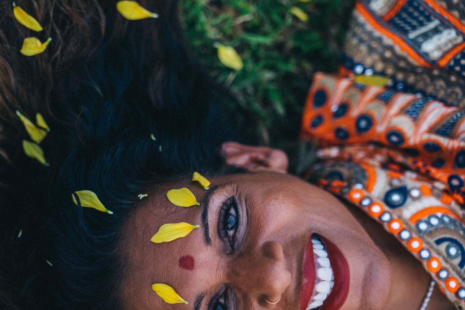 Close-up of smiling Indian woman in traditional saree, with yellow petals in hair. Vibrant and joyful outdoor scene.